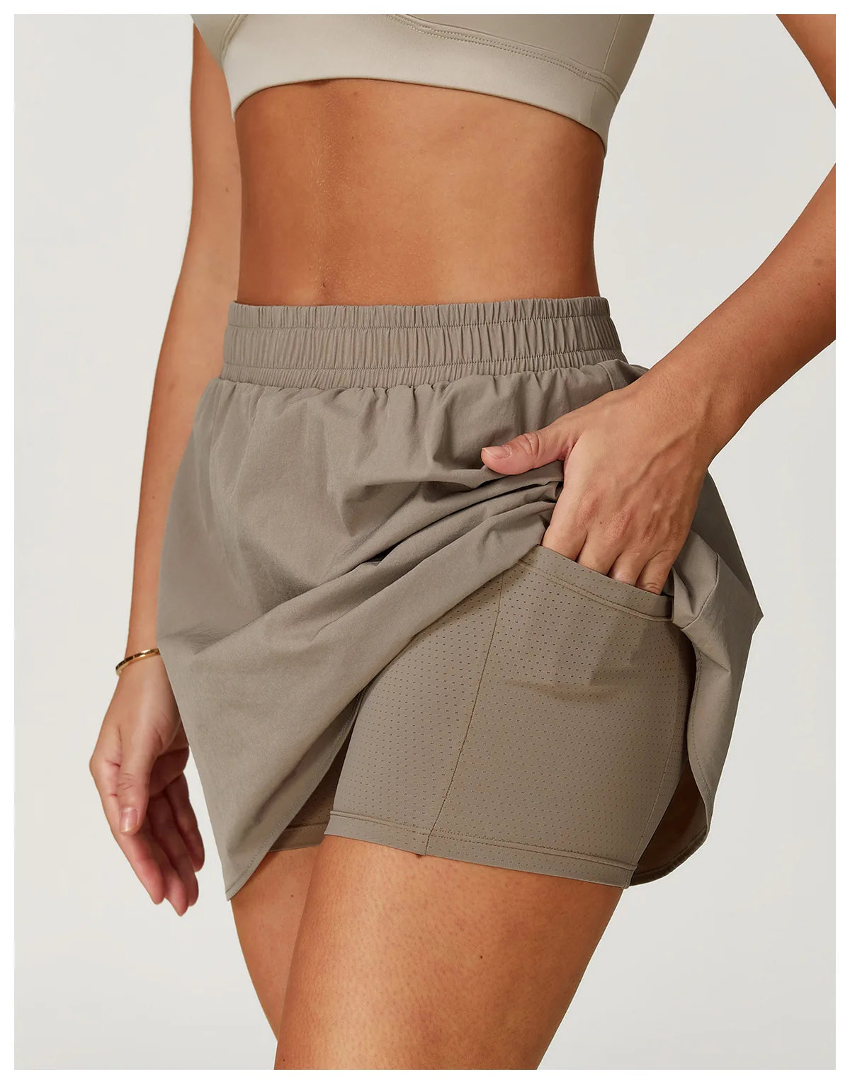 Woman wearing taupe athletic skort with built-in perforated shorts and crop top