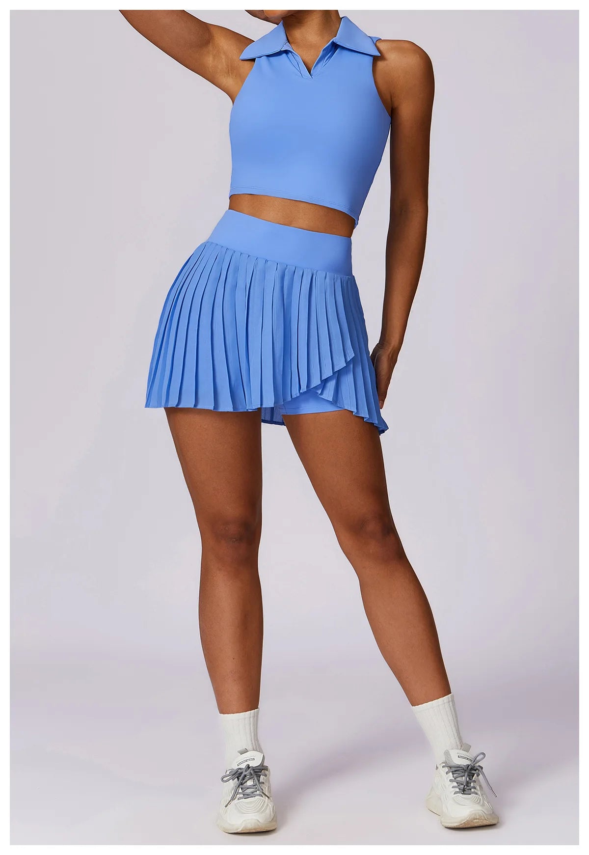 Woman in light blue pleated tennis skirt and collared crop top with sneakers