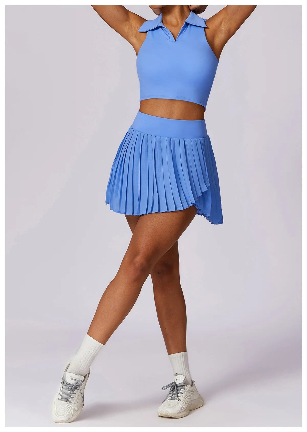 Woman wearing blue pleated tennis skirt and collared crop top with white sneakers