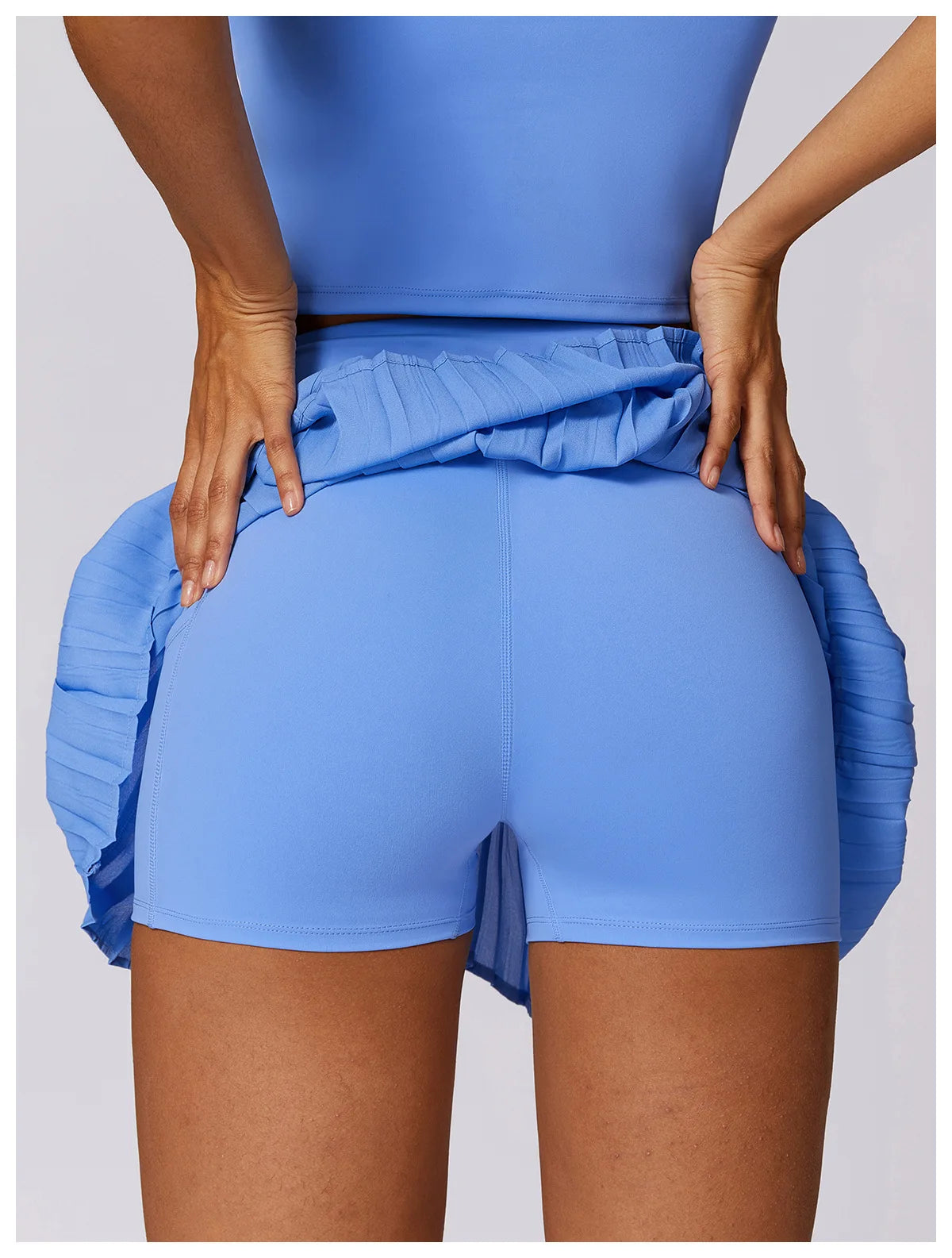 Woman in blue athletic shorts and pleated skirt, hands on hips, fitness apparel