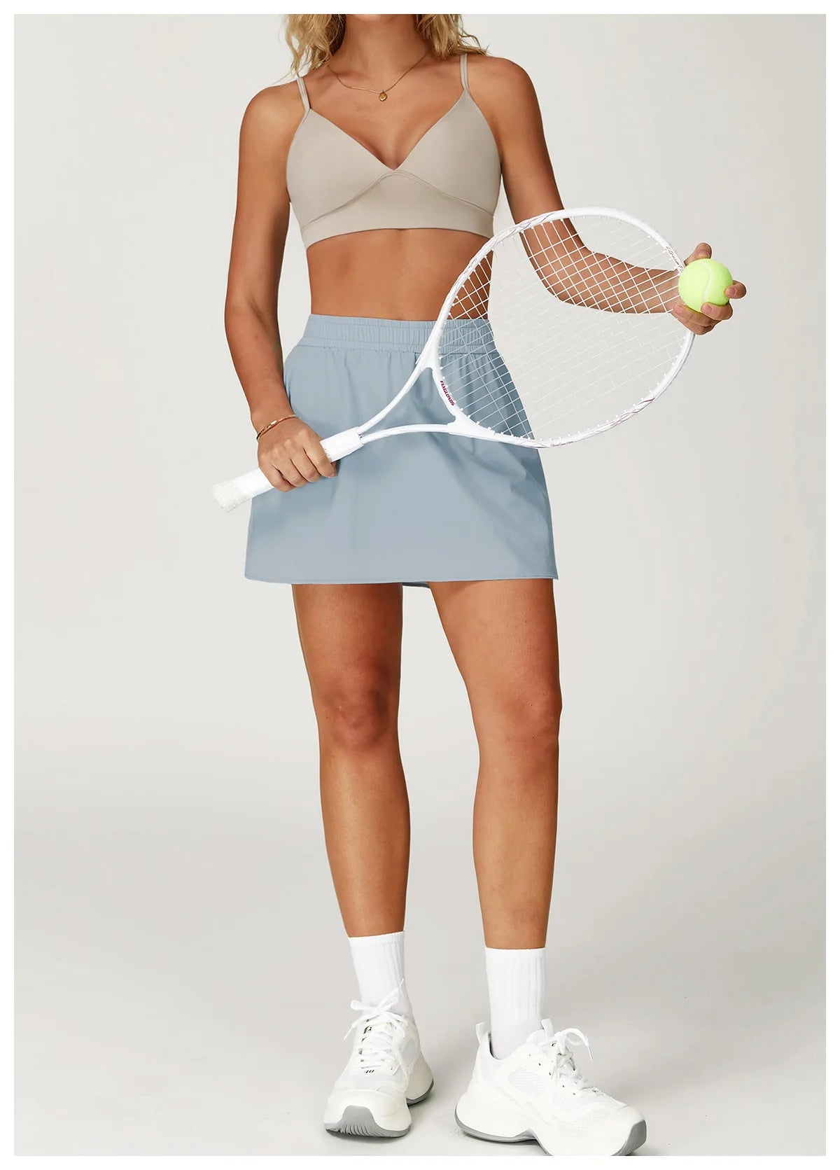 Woman in activewear sports bra and blue tennis skirt holding racket and tennis ball