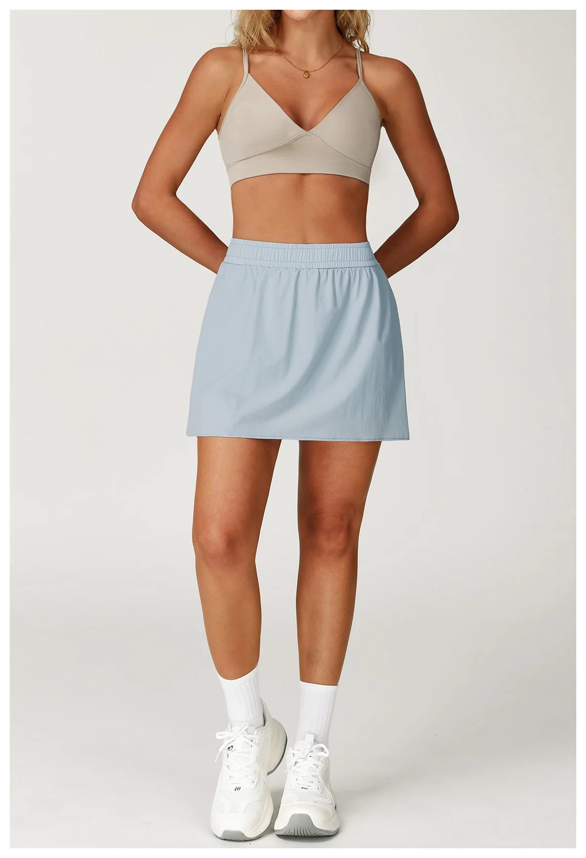 Woman wearing light blue athletic skirt, beige sports bra, white sneakers and socks