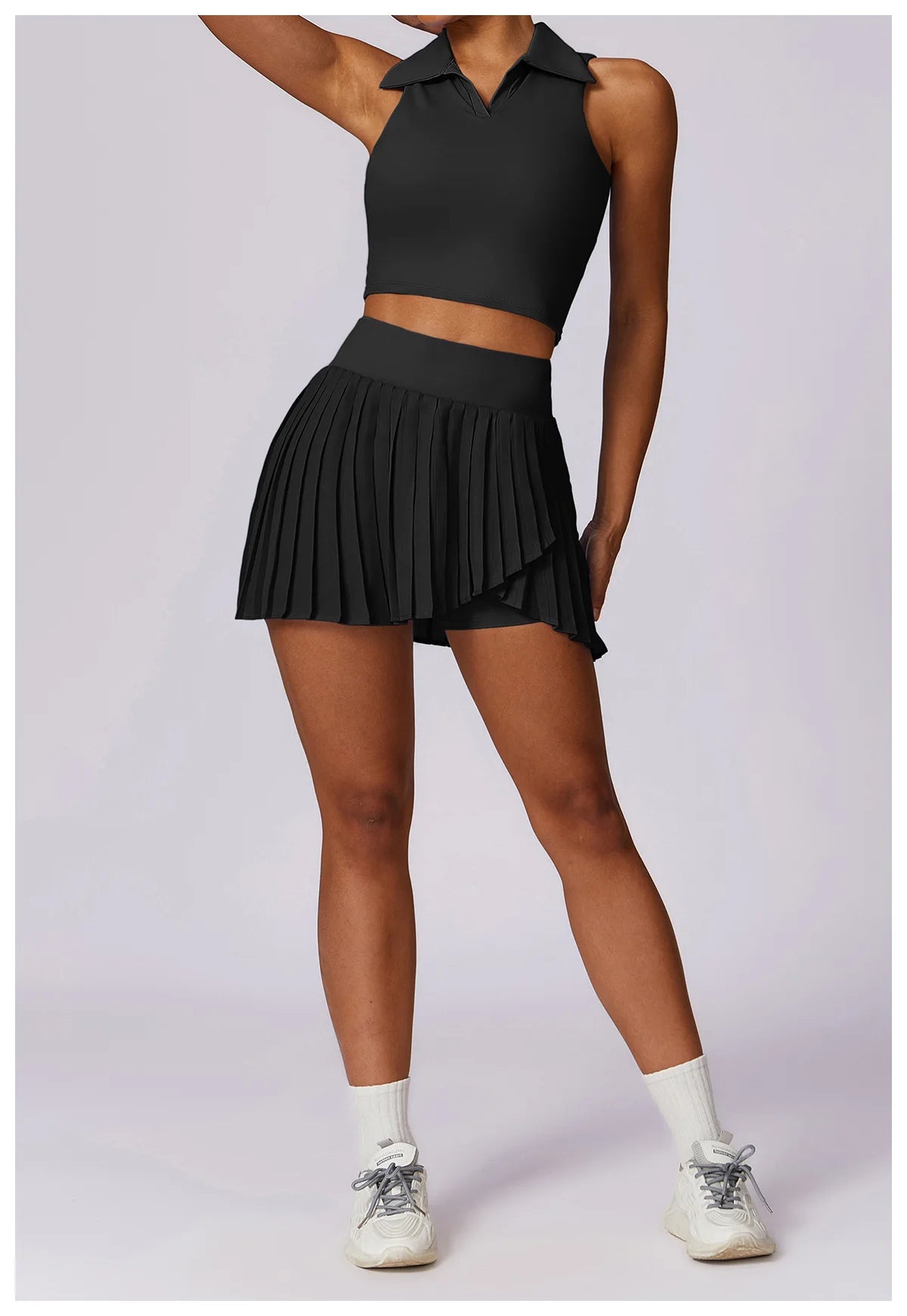 Woman wearing black sleeveless collared crop top and pleated tennis skirt set