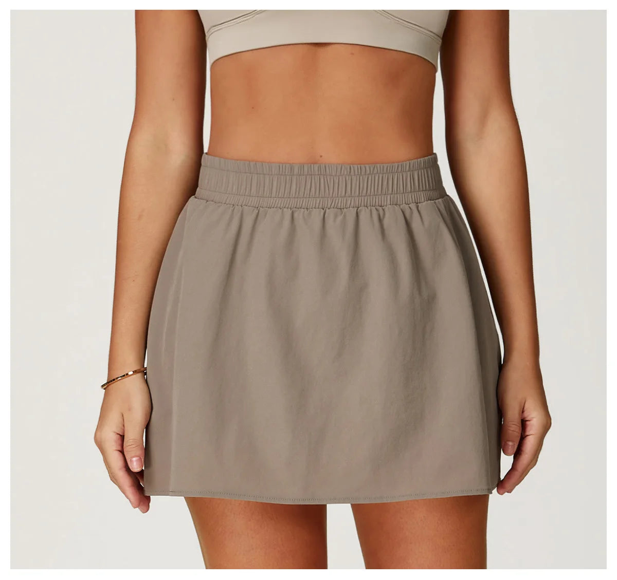 Woman wearing taupe athletic mini skirt with elastic waistband and crop top